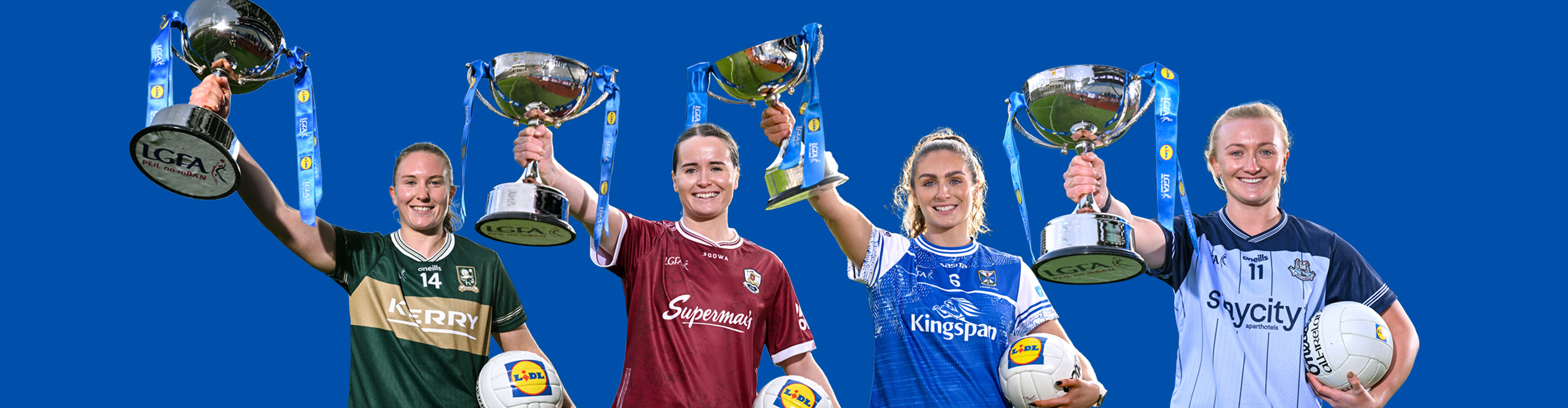 Four female athletes in jerseys holding up trophies and footballs.
