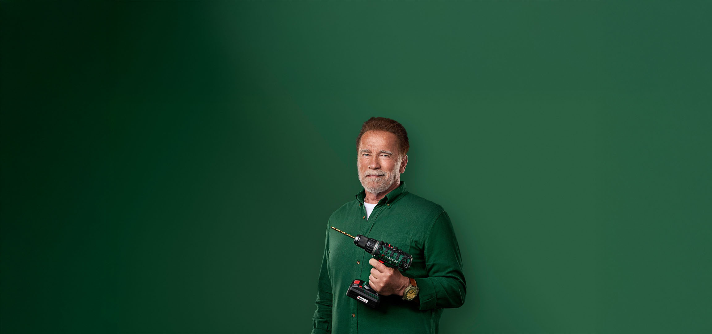 Arnold Schwarzenegger holding a Parkside drill against a green background.