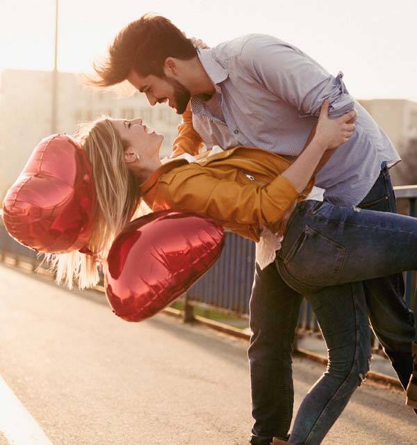 A couple holding heart-shaped balloons, embracing and smiling outdoors.